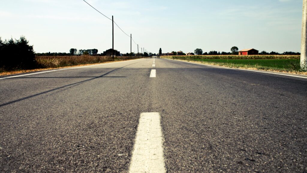 A tranquil countryside road in Calderara di Reno, Italy, with clear blue skies and open fields.